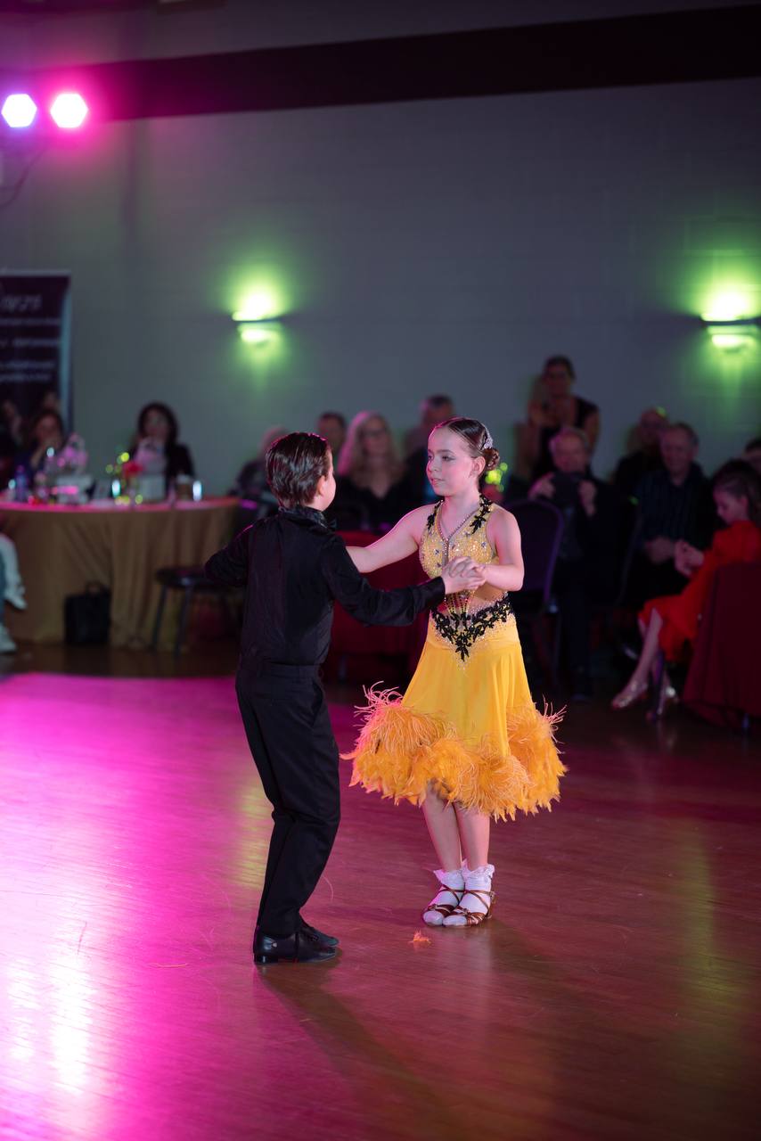 Young ballroom partners holding hands beneath colourful lights